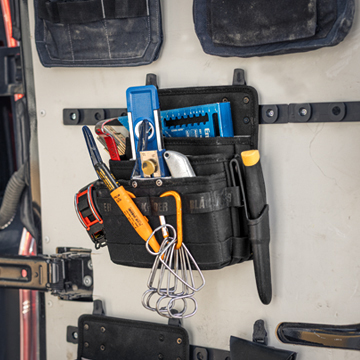Blåkläder ToolRig tool pouch mounted on a wall, holding hand tools such as pliers, screwdrivers, and measuring tools in an organized setup.