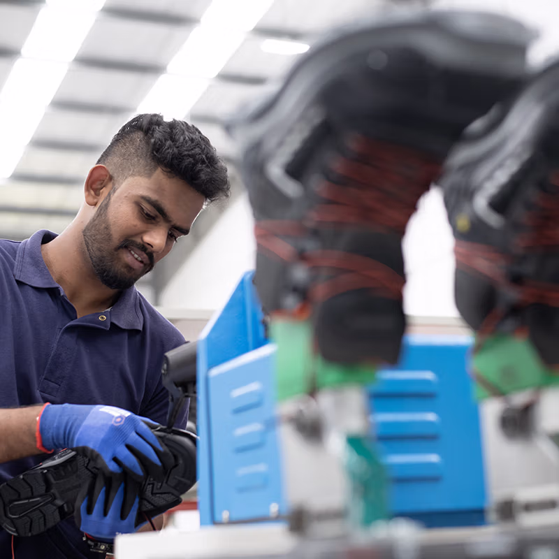 Worker inspecting and assembling safety shoes in a modern production facility, ensuring quality, precision and durability built for demanding work environments.