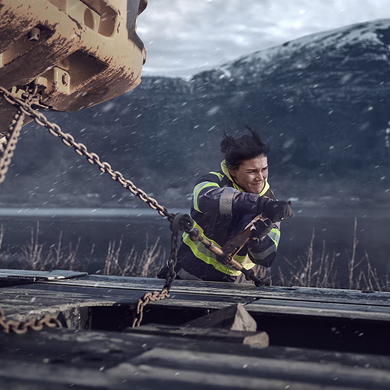 High-visibility workwear in action as a worker secures heavy load chains on a truck in harsh weather—designed for durability, safety and performance in the toughest conditions.