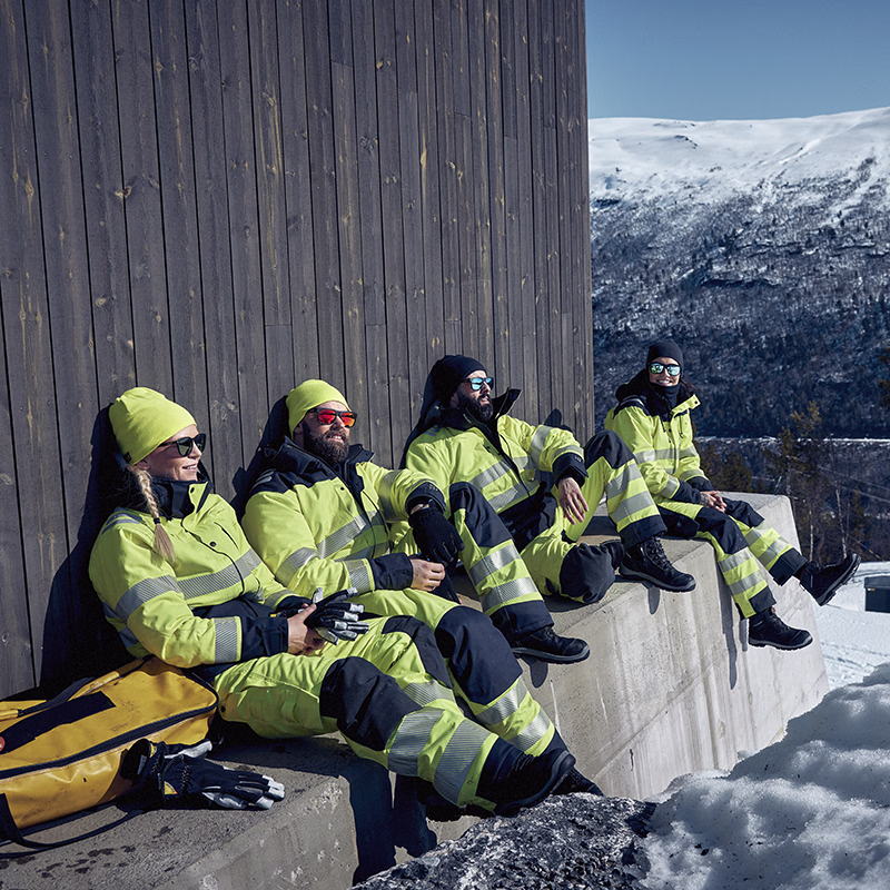 Team of workers in high-visibility workwear taking a break outdoors in snowy conditions, set against a mountainous landscape—designed to deliver protection, comfort and performance in cold, demanding environments.